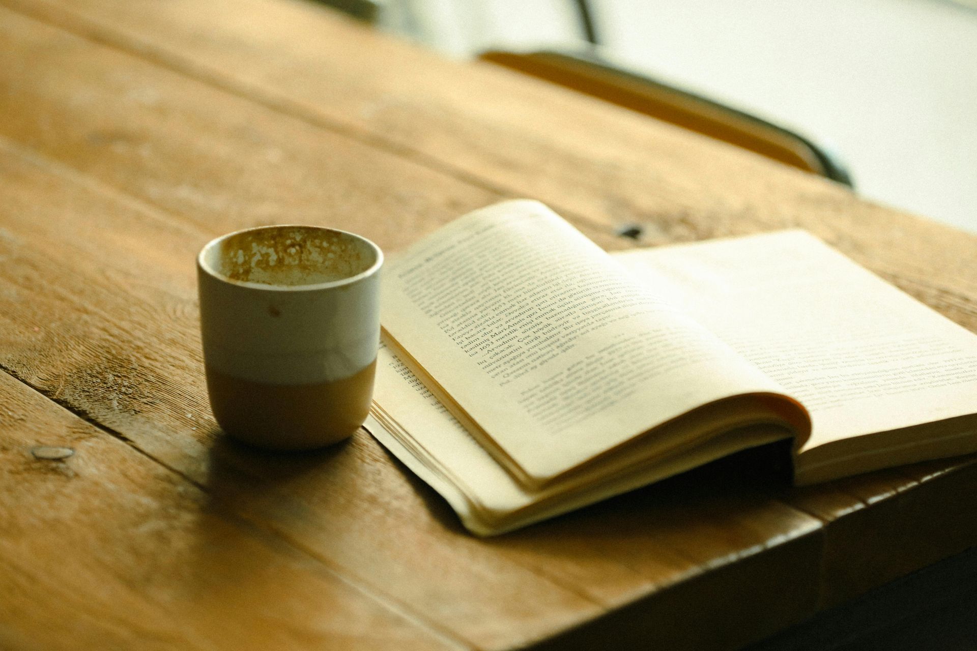 A coffee cup beside an open book on a wooden table
