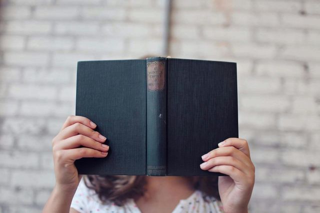 A woman is covering her face with an open book.